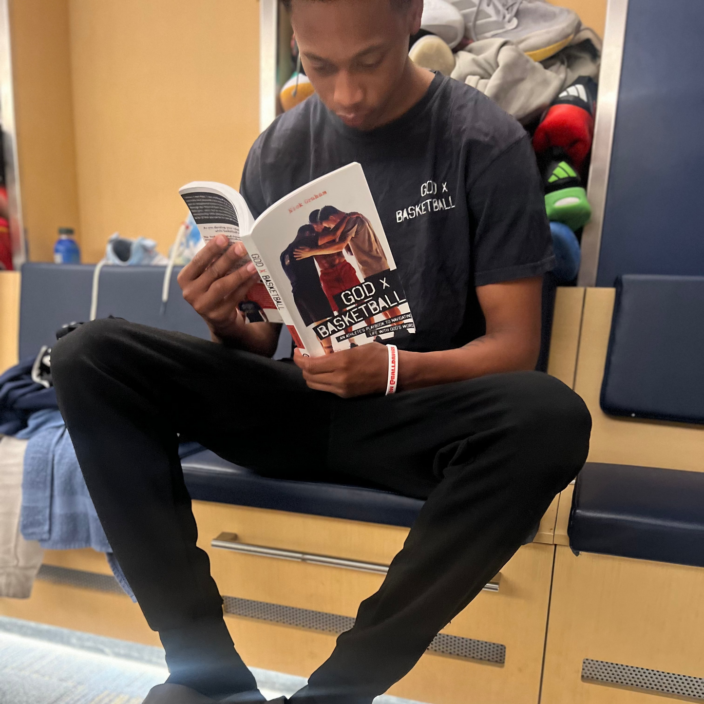 Person reading a book about basketball with a basketball at their feet in a waiting area.